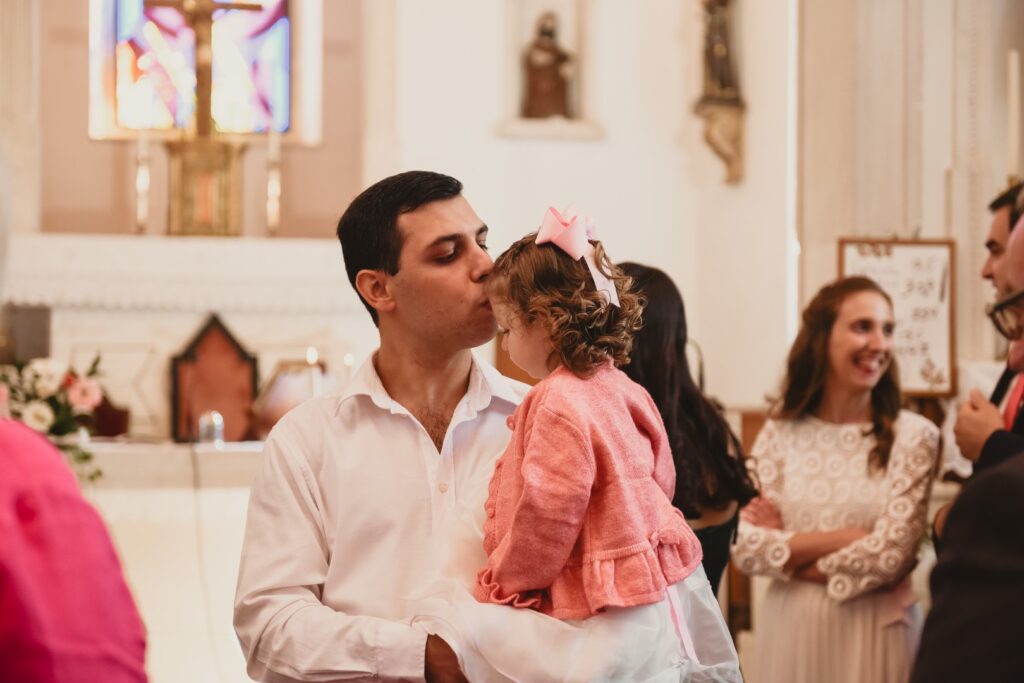 Fotografia de Batizado. Pai pega menina ao colo. Interior da igreja.