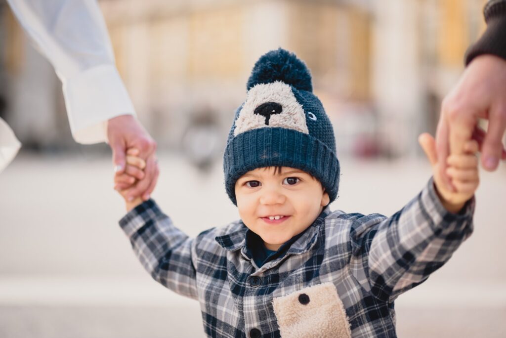 Sessões fotográficas de família. Sessões fotográficas em exterior, em Lisboa. Pormenor de rosto do filho, com cada uma das mãos dadas ao pai e à mãe.