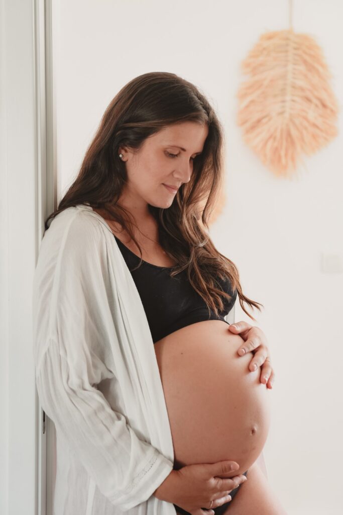 Sessões fotográficas gravidez. Mulher grávida que olha feliz para a barriga. Sessões fotográficas de gravidez em casa.